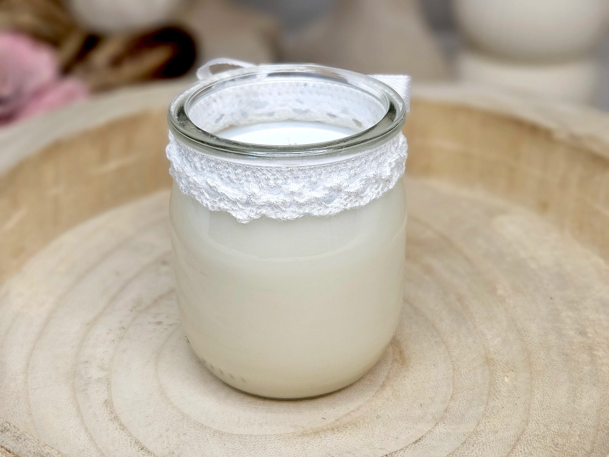 Vue de dosd'une bougie artisanale lait de riz avec son nœud en satin blanc et sa bordure en dentelle délicate.