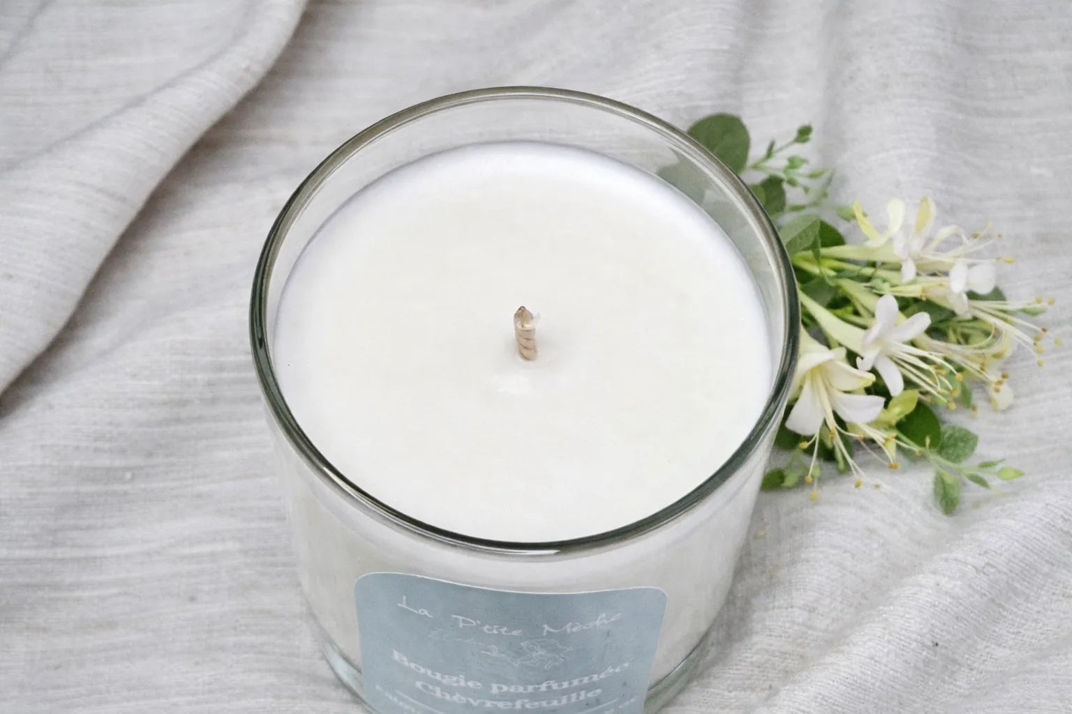 Vue du dessus d'une bougie blanche au Chèvrefeuille avec fleurs fraîches en arrière-plan, fabrication française à la main