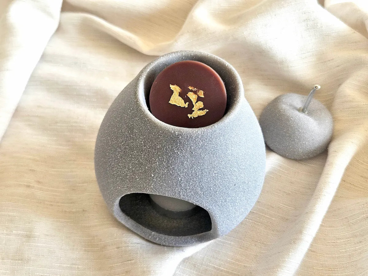Fondant parfumé à la noix de coco déposé dans la coupelle d'un brûleur design gris, prêt pour une diffusion gourmande et poudrée.