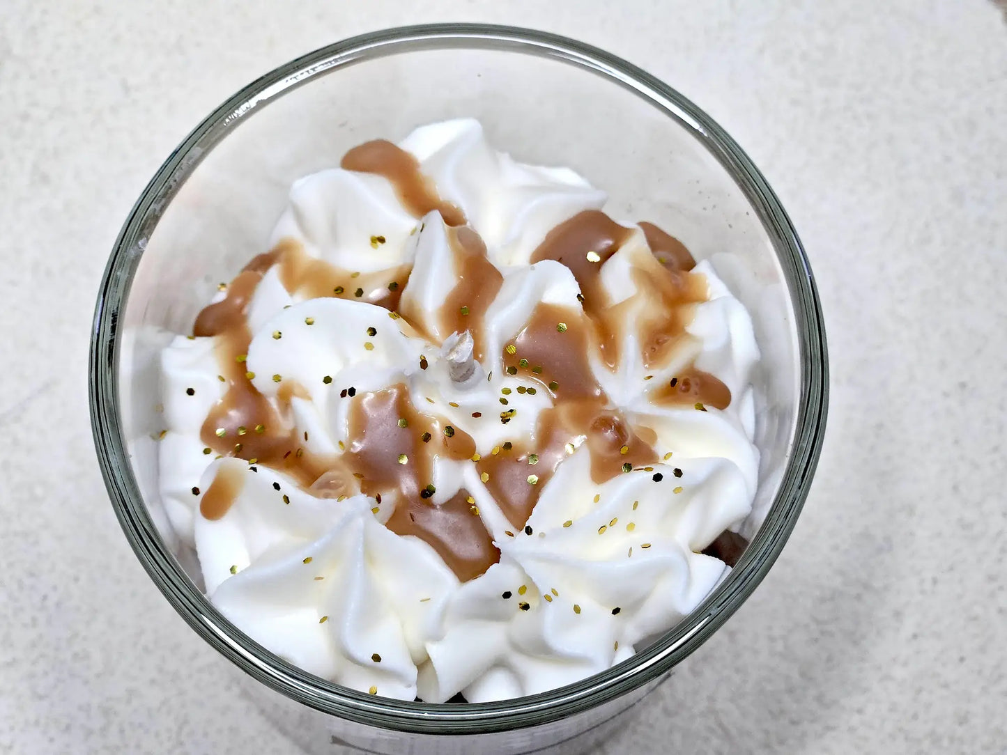 Gros plan sur le coulis en cire et les éclats décoratifs sur le dôme d'une bougie gourmande à la madeleine.