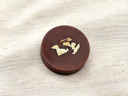 Palet fondant parfumé à la Noix de Coco, couleur brun intense avec éclats de feuille d'or, posé sur un lin clair texturé.