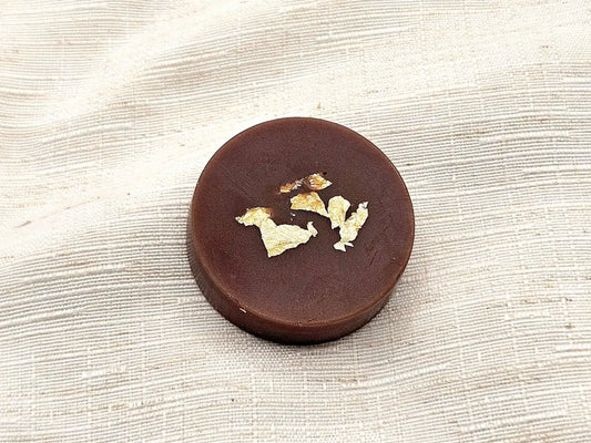 Palet fondant parfumé à la Noix de Coco, couleur brun intense avec éclats de feuille d'or, posé sur un lin clair texturé.