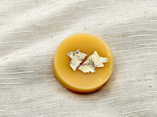 Palet fondant parfumé à la Vanille des Îles, couleur jaune miel avec éclats de feuille d'or, posé sur un tissu de lin blanc.