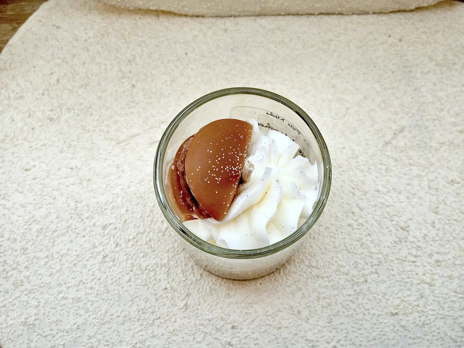 Focus sur la mèche coton et le mini macaron décoratif d'une bougie parfumée aux notes de pâtisserie fine.
