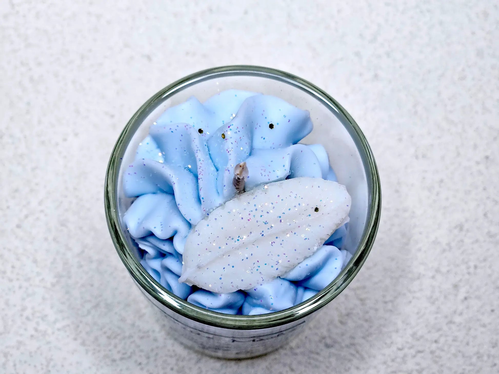 Détail de la mèche coton et des décors délicats sur une petite bougie gourmande aux notes de fleurs blanches.